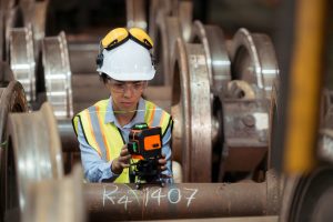 Railway technician in uniform and helmet inspect the train wheel Railway technician in uniform and helmet inspect the train wheels removed from the locomotives in the train workshop.